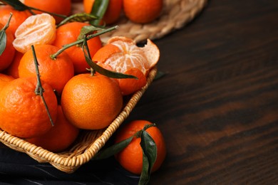 Photo of Fresh ripe tangerines with green leaves in wicker basket on wooden table, closeup. Space for text