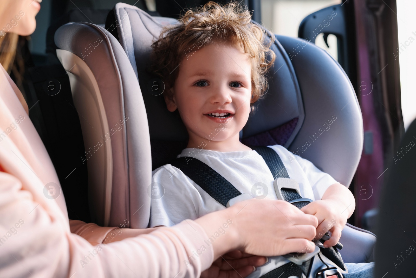 Photo of Mother fastening her son in child safety seat inside car