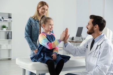 Photo of Happy mother and daughter having appointment with doctor. Pediatrician and patient giving high five in clinic