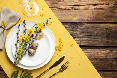 Festive Easter table setting with quail eggs and floral decor on wooden background, flat lay. Space for text