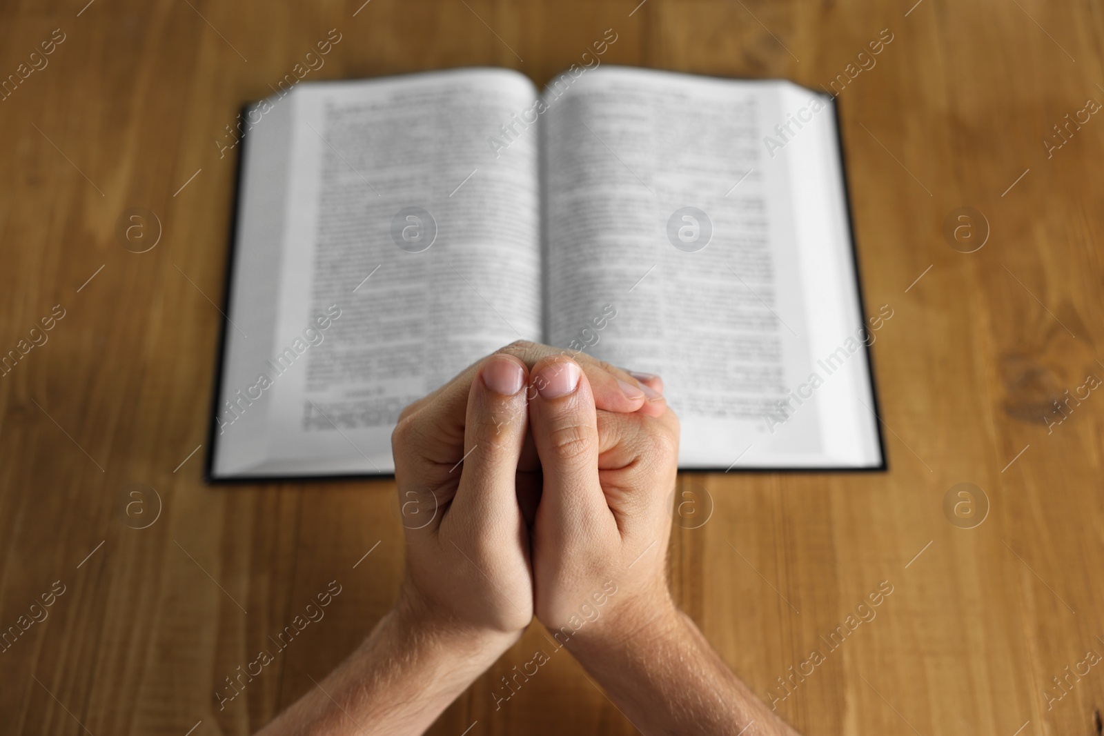 Photo of Man with Bible praying at wooden table, closeup