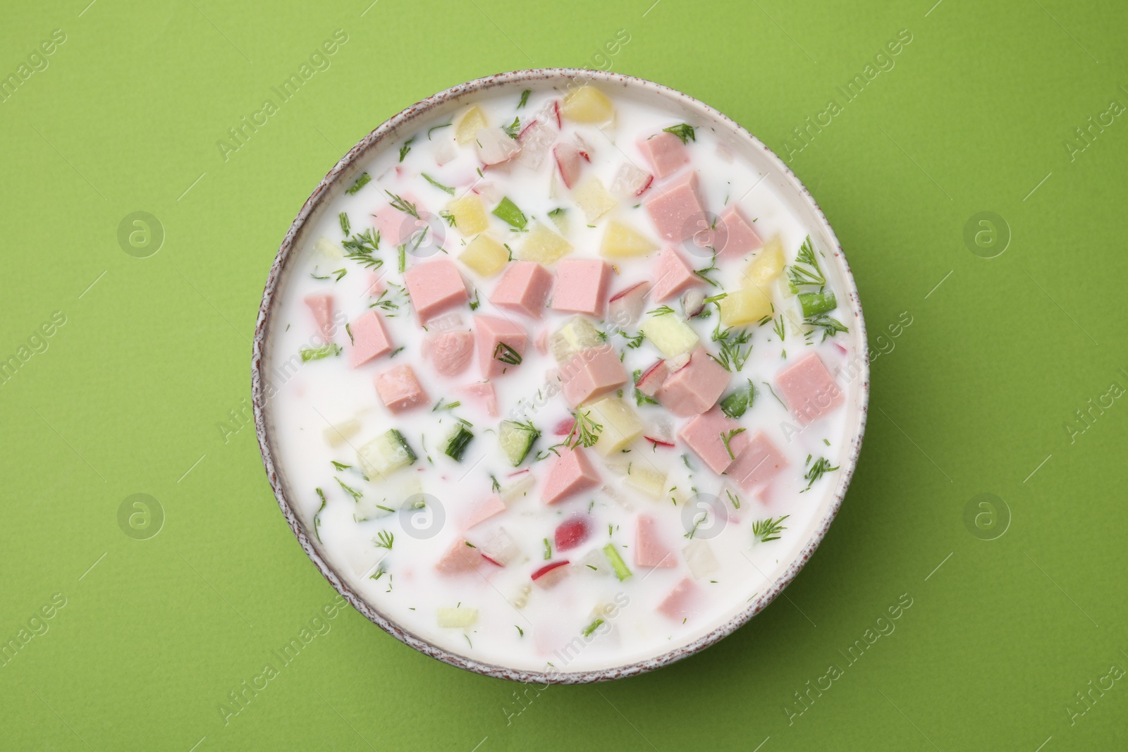 Photo of Delicious cold summer soup (okroshka) with boiled sausage in bowl on green table, top view