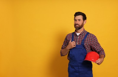Photo of Professional builder with hard hat on yellow background, space for text