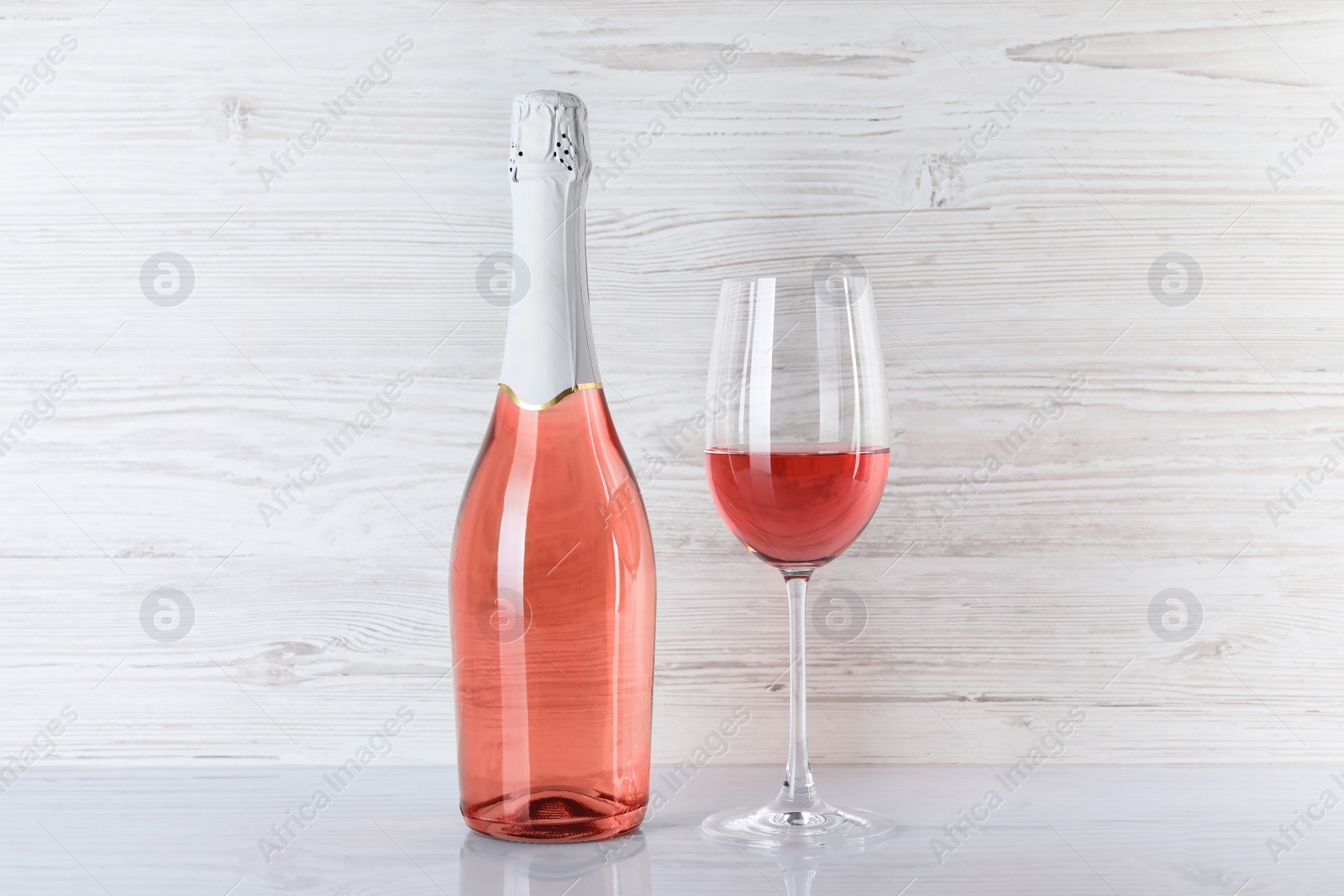 Photo of Bottle and glass of delicious rose wine on table against white wooden background