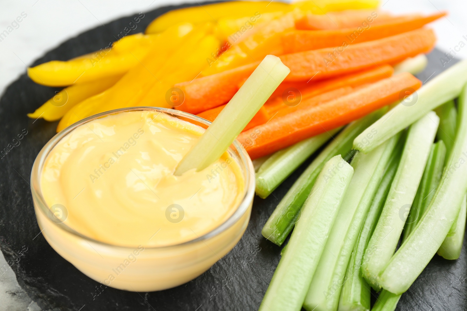 Photo of Celery and other vegetable sticks with dip sauce on slate plate, closeup