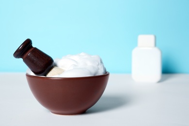 Photo of Dish with shaving brush and foam on white table. Space for text