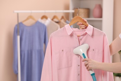 Woman steaming shirt on hanger at home, closeup. Space for text