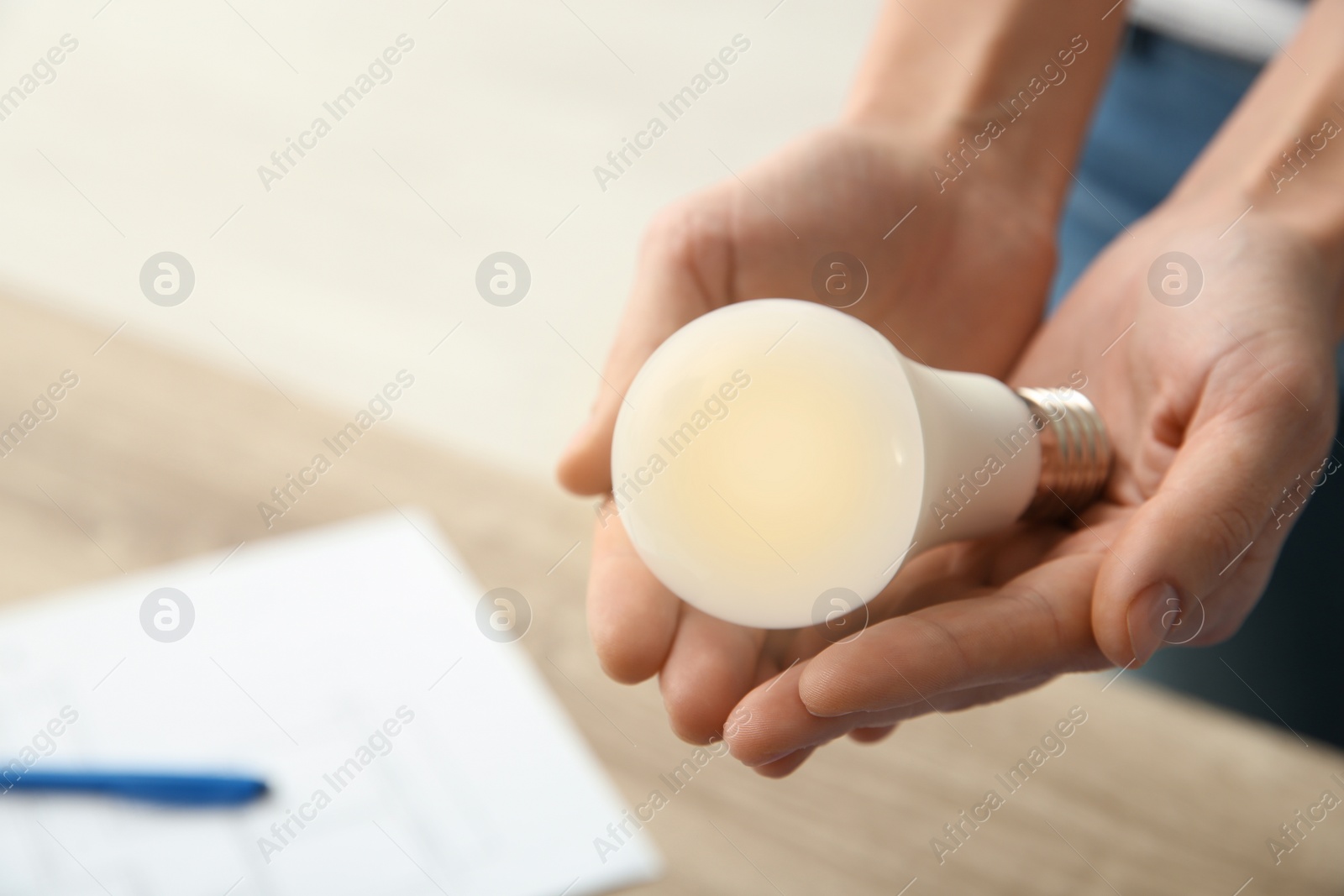 Photo of Woman holding lamp bulb on blurred background, closeup with space for text