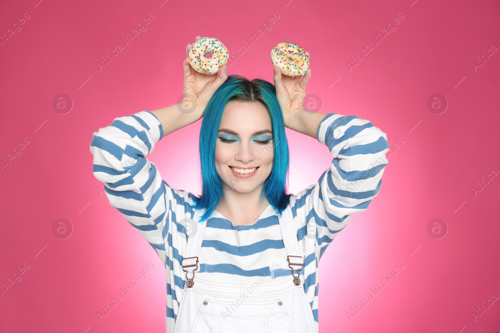 Photo of Young woman with bright dyed hair holding donuts on pink background