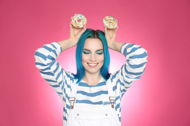 Young woman with bright dyed hair holding donuts on pink background