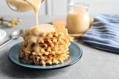 Photo of Pouring condensed milk from jug onto waffles on grey table, space for text. Dairy product