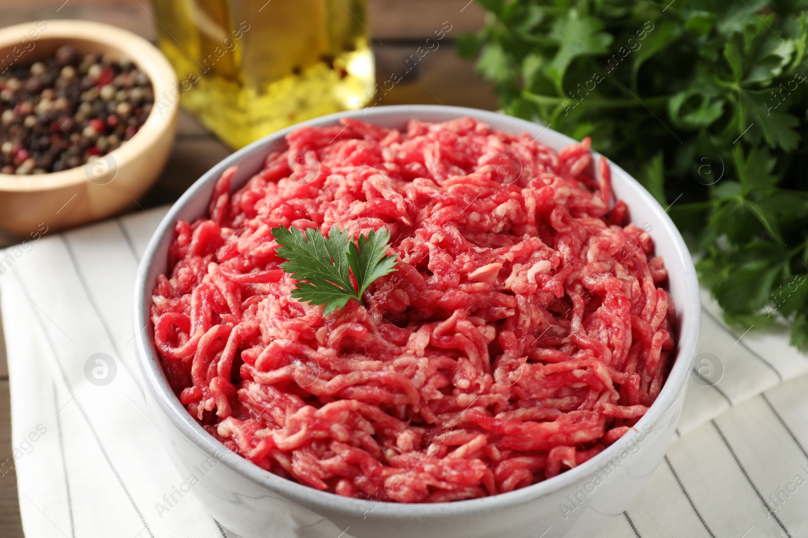 Photo of Raw ground meat in bowl, parsley, spices and oil on table, closeup