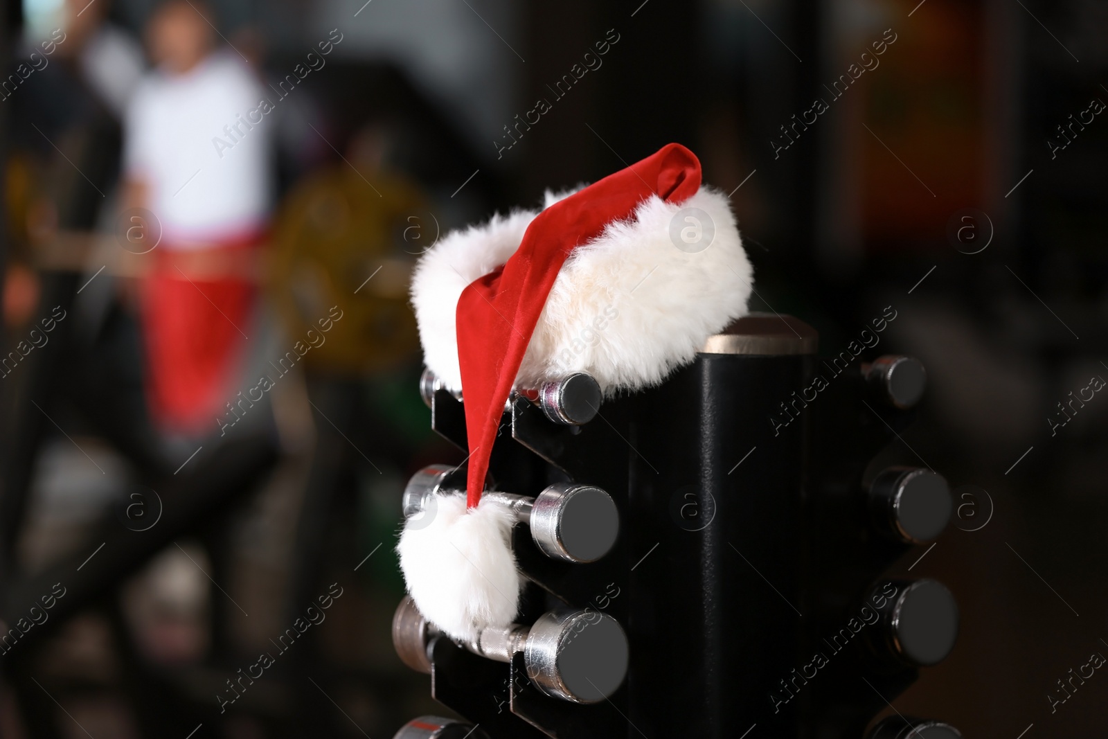 Photo of Santa Claus hat on stand with dumbbells in gym