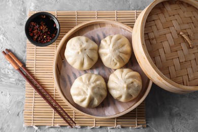 Photo of Delicious bao buns (baozi), chopsticks and sauce on grey textured table, flat lay