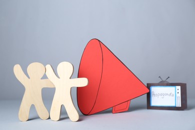 Photo of Propaganda concept. Wooden figures near big paper megaphone and TV on light grey background