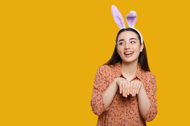 Photo of Happy woman wearing bunny ears headband on orange background, space for text. Easter celebration