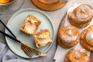 Photo of Delicious profiteroles filled with cream on grey table, flat lay