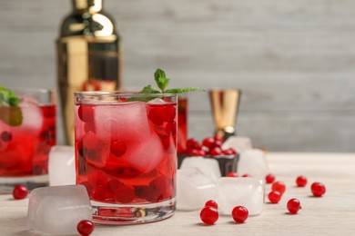 Tasty cranberry cocktail with ice cubes in glass and fresh berries on wooden table, space for text