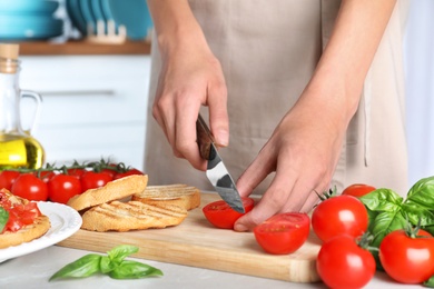Photo of Woman cutting tomato for bruschettas at light grey marble table, closeup