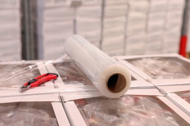 Roll of stretch film and utility knife on wrapped boxes in warehouse