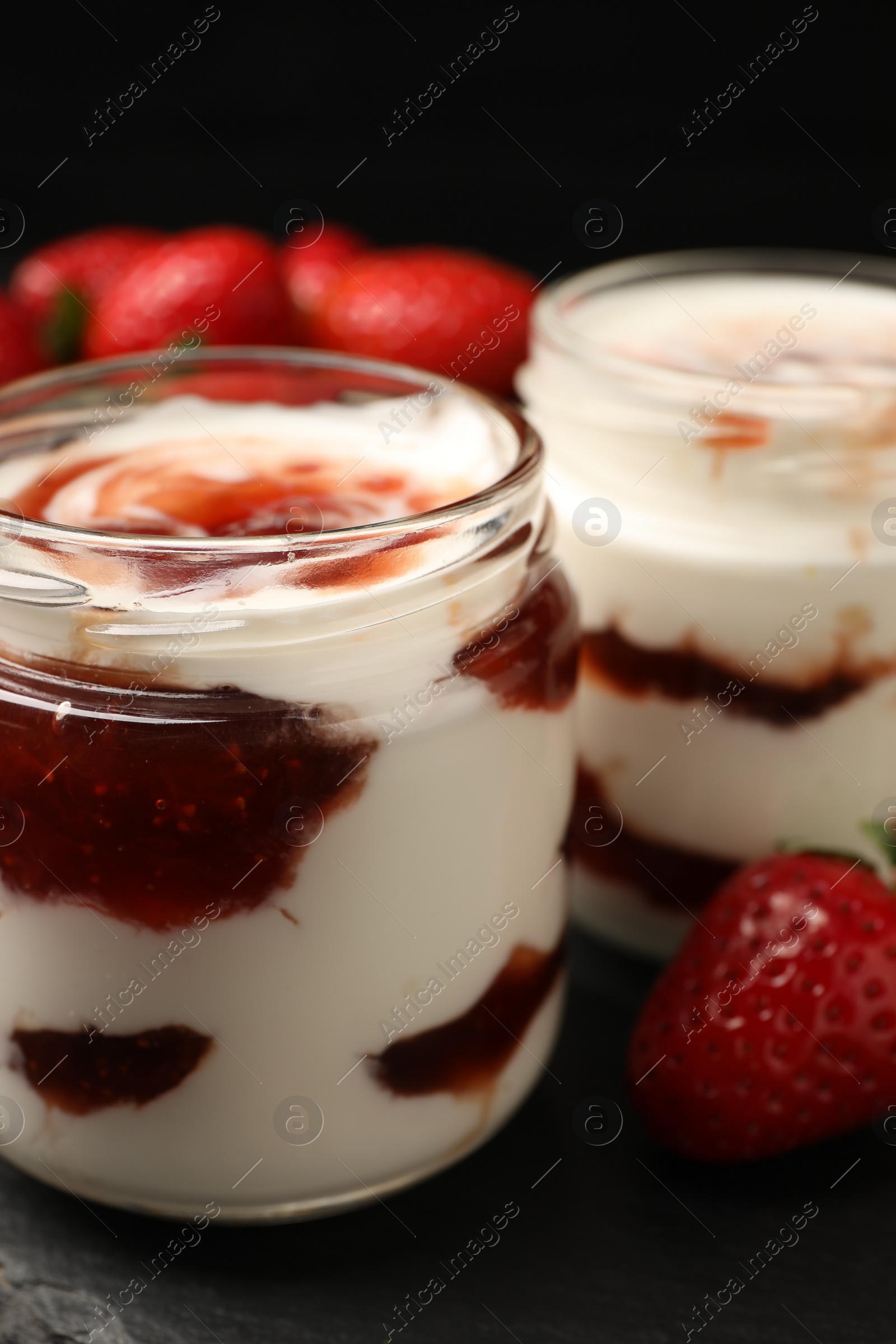 Photo of Tasty yoghurt with jam and strawberries on black table, closeup