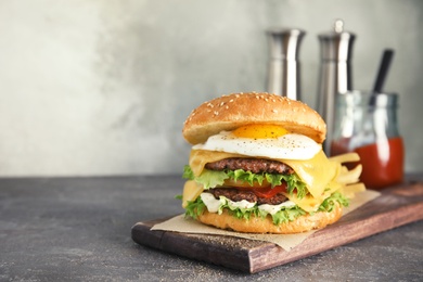 Tasty burger with fried egg on wooden board, space for text