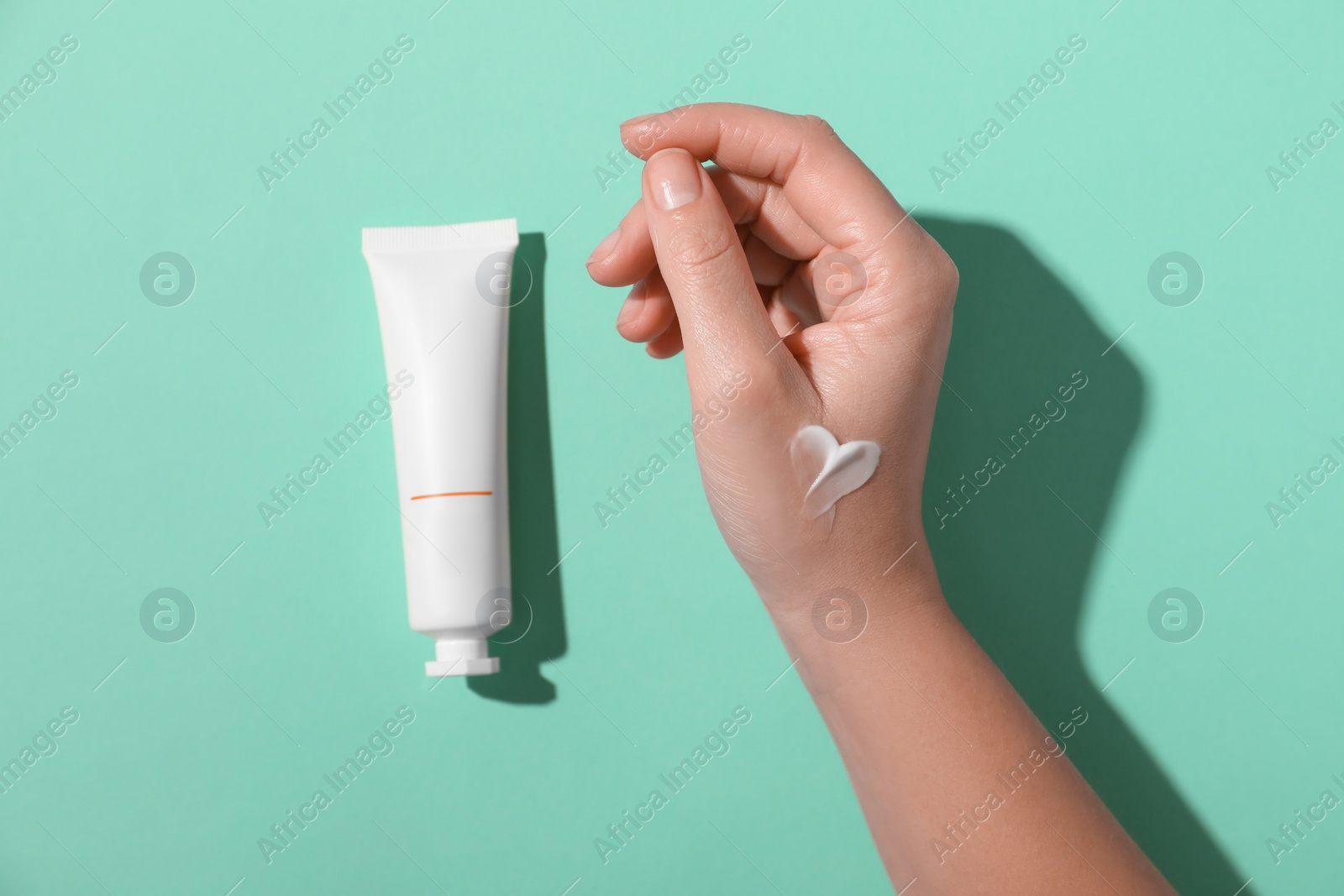 Photo of Woman with tube of hand cream on turquoise background, top view