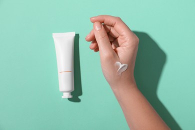 Photo of Woman with tube of hand cream on turquoise background, top view