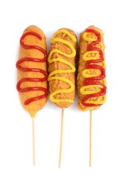 Photo of Delicious deep fried corn dogs with sauces on white background, top view
