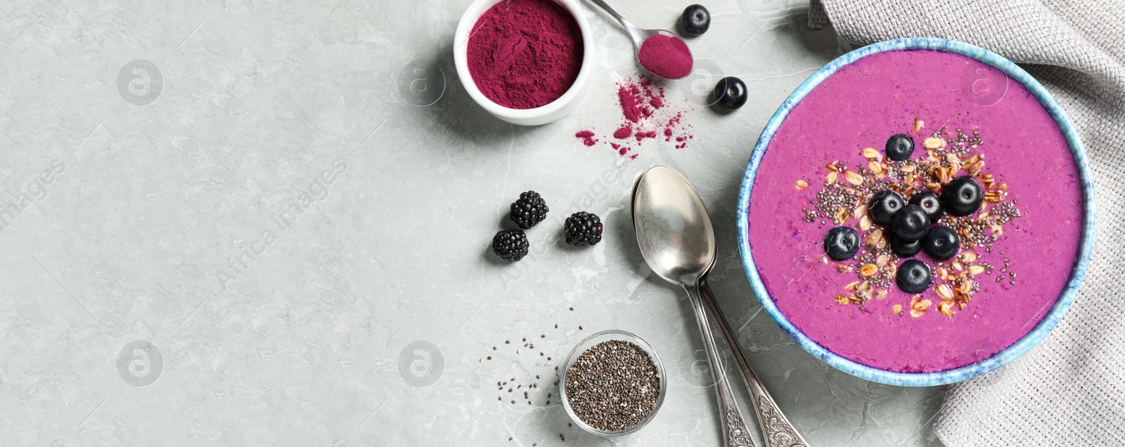 Photo of Delicious acai smoothie with granola and chia seeds served on grey table, flat lay. Space for text