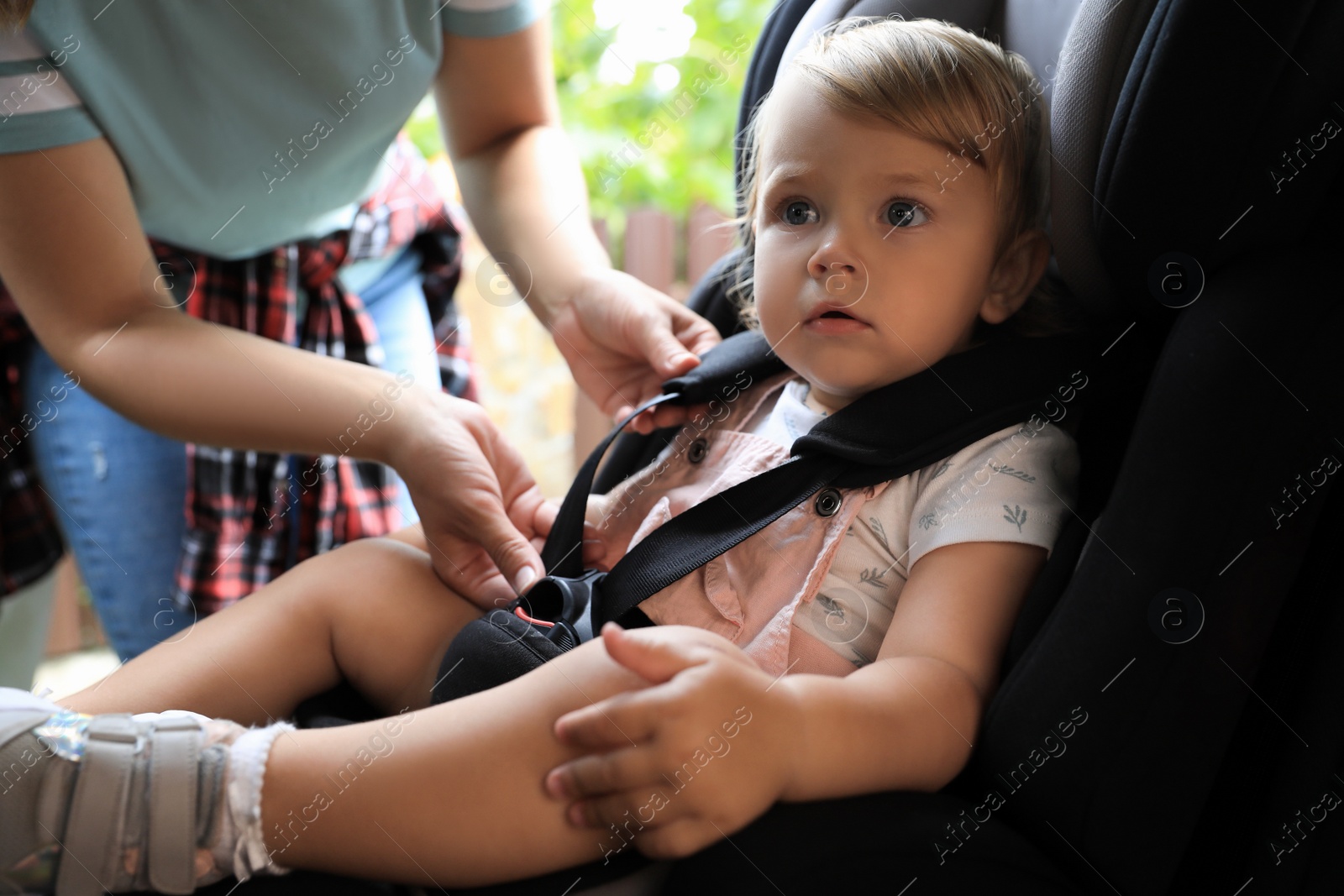 Photo of Mother fastening her daughter in child safety seat inside car