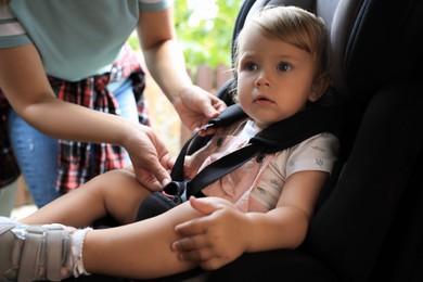 Mother fastening her daughter in child safety seat inside car