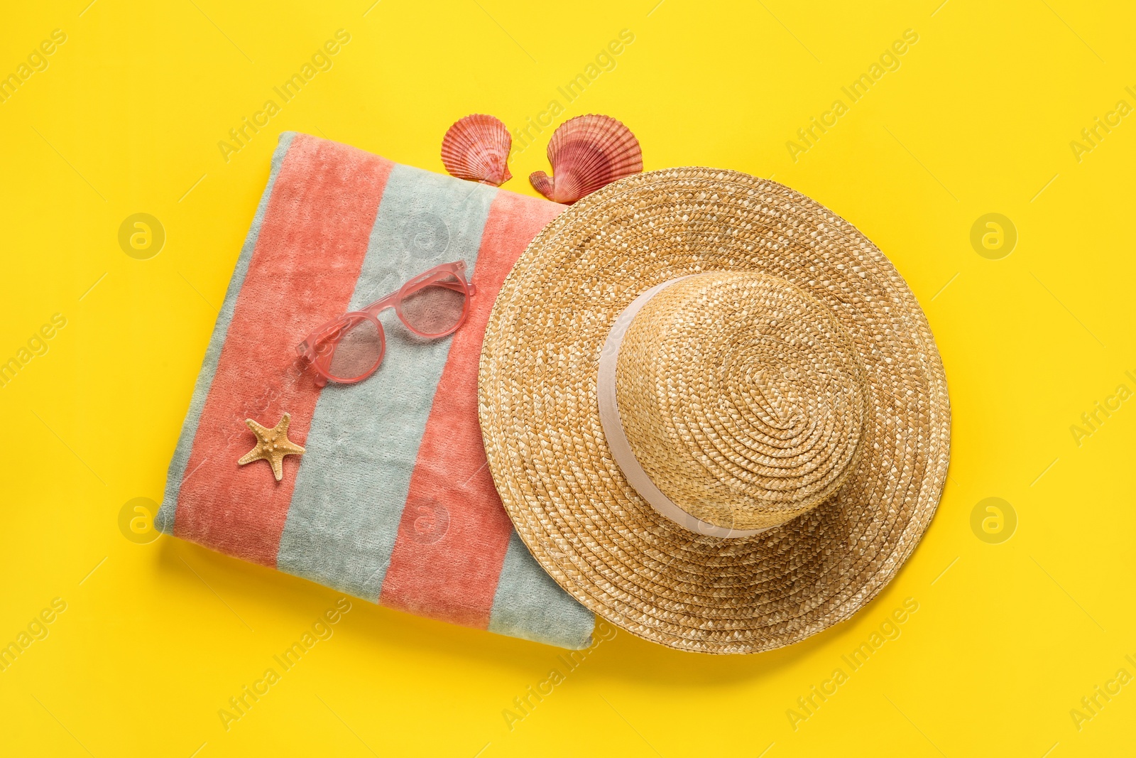 Photo of Beach towel, straw hat and sunglasses on yellow background, flat lay