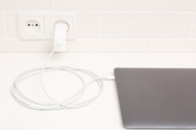 Charging laptop with power adapter in electrical socket on white table