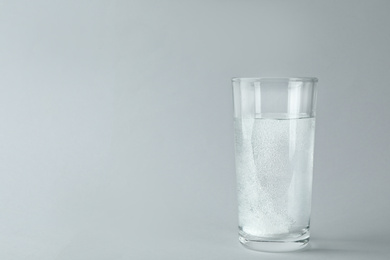 Photo of Glass of water with effervescent tablet on light grey background, space for text