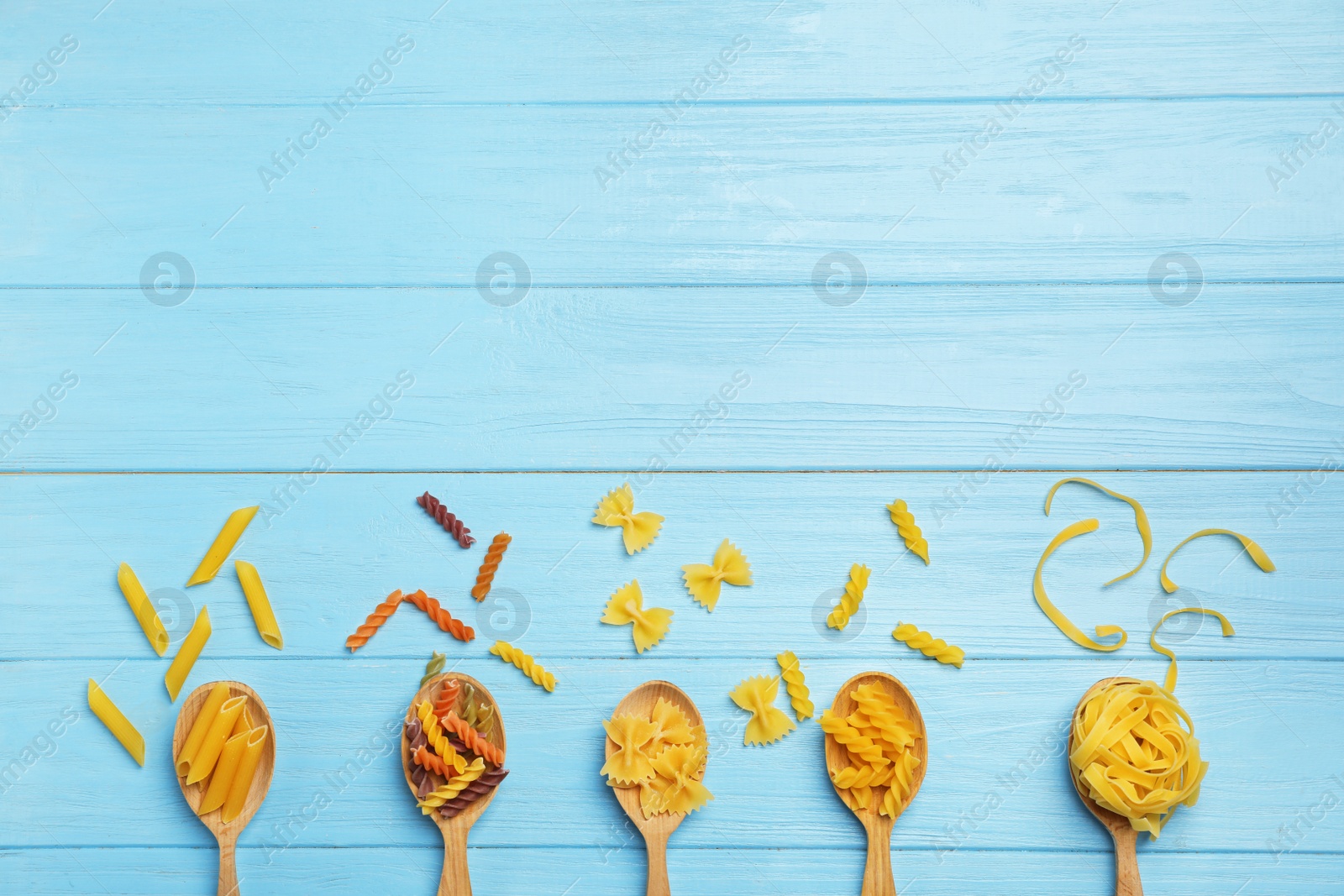 Photo of Spoons with different raw pasta on wooden background, top view