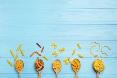 Spoons with different raw pasta on wooden background, top view