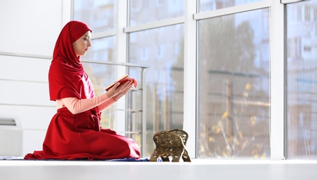 Photo of Muslim woman in hijab reading Koran indoors. Space for text