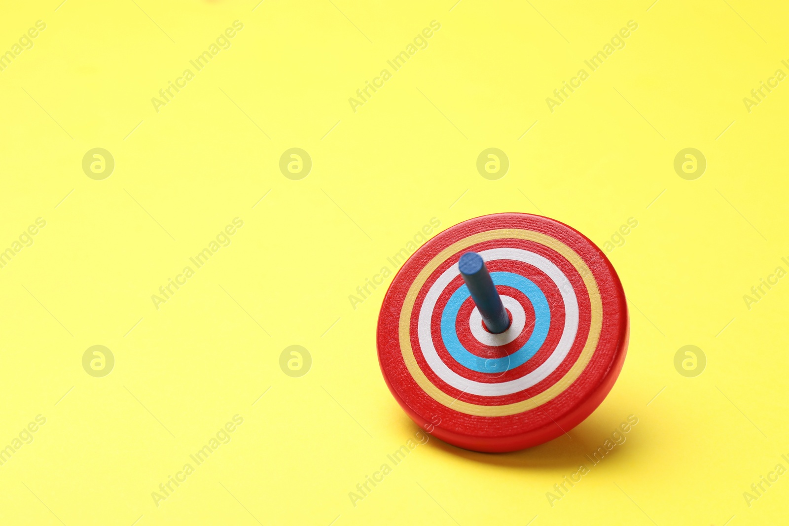 Photo of One colorful spinning top on yellow background, space for text