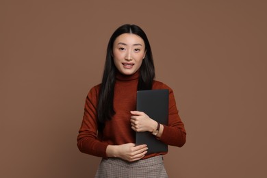 Portrait of smiling woman with laptop on brown background