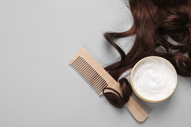 Photo of Lockhealthy brown hair, comb and cosmetic product on light grey background, flat lay. Space for text