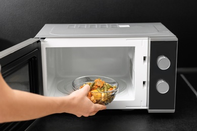 Young woman using microwave oven on table in kitchen