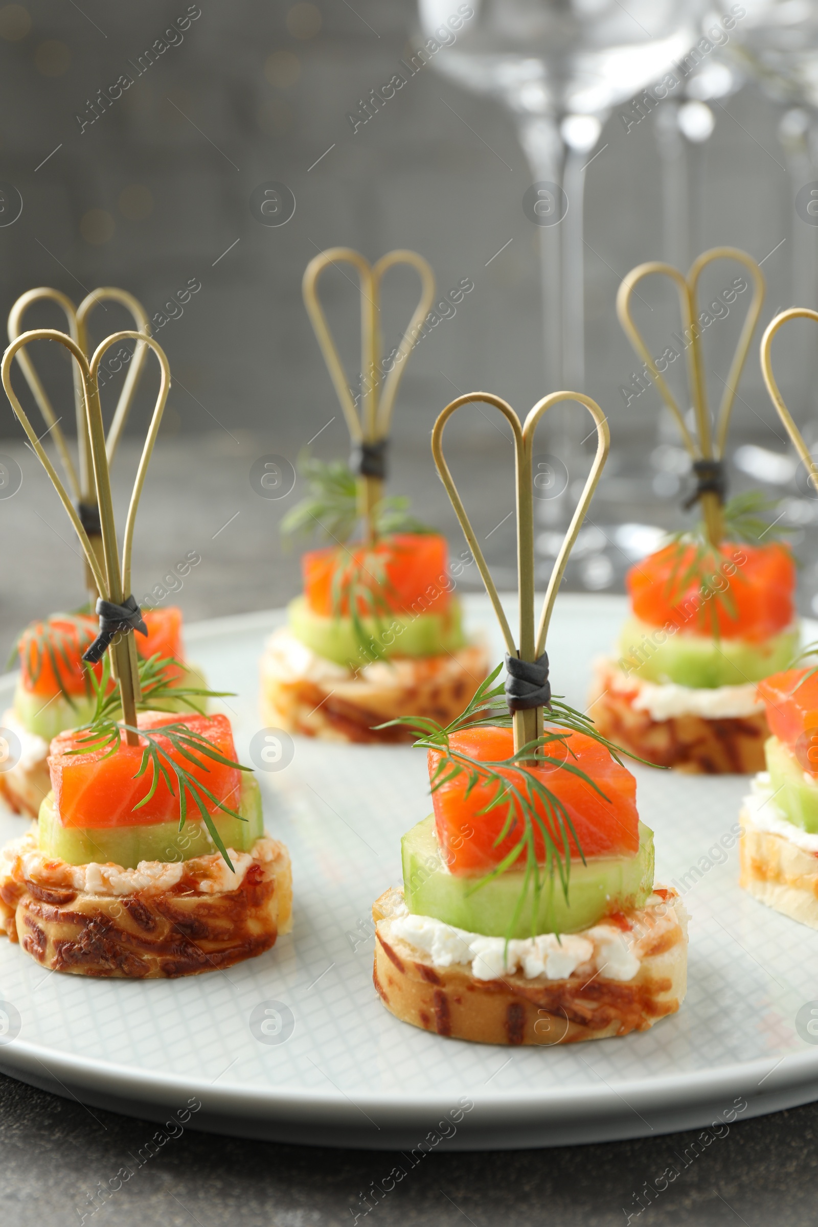 Photo of Tasty canapes with salmon, cucumber, bread and cream cheese on grey table, closeup