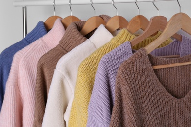 Photo of Warm sweaters hanging on rack against white background, closeup