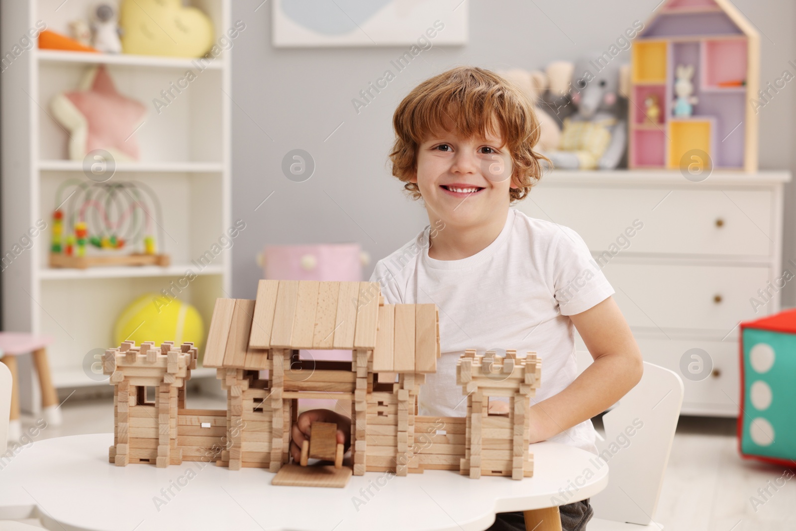 Photo of Little boy playing with wooden entry gate and car at white table in room. Child's toys