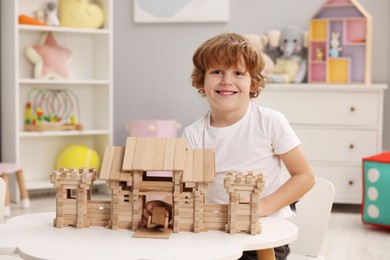 Little boy playing with wooden entry gate and car at white table in room. Child's toys
