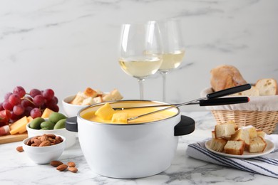 Photo of Tasty cheese fondue, snacks and wine on white marble table