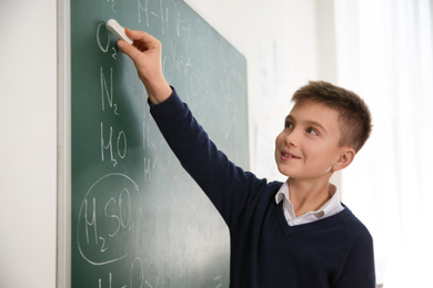 Photo of Schoolboy writing chemical formulas on chalkboard in classroom