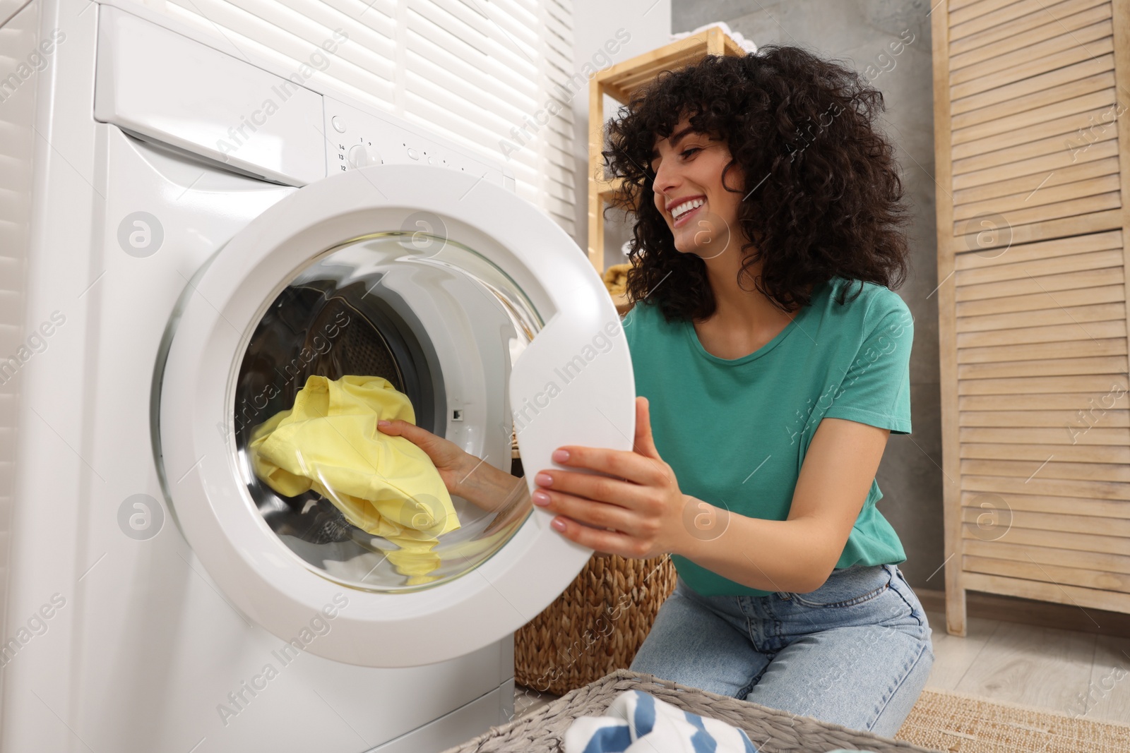 Photo of Happy woman putting laundry into washing machine indoors