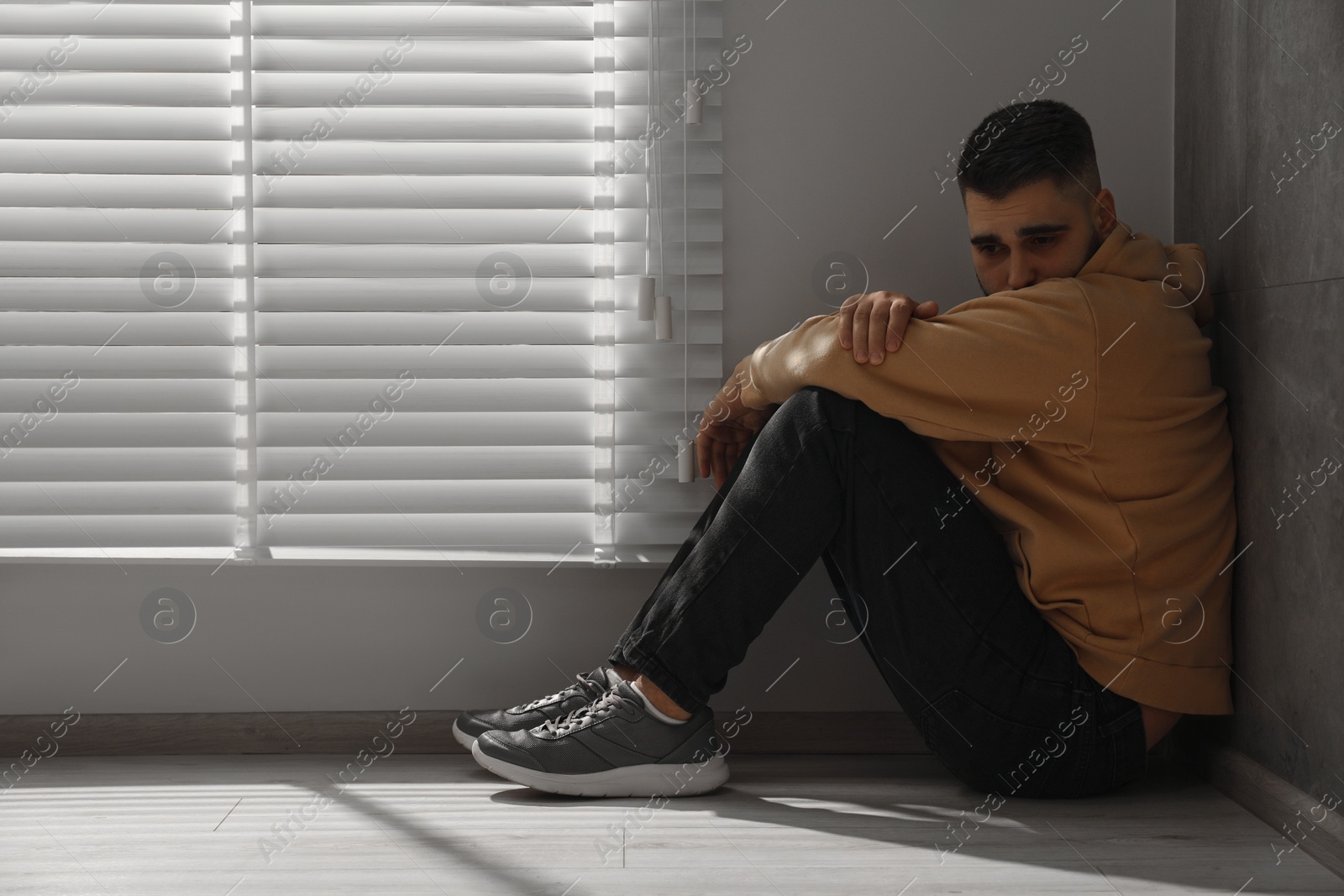 Photo of Sad man sitting on floor near window. Space for text